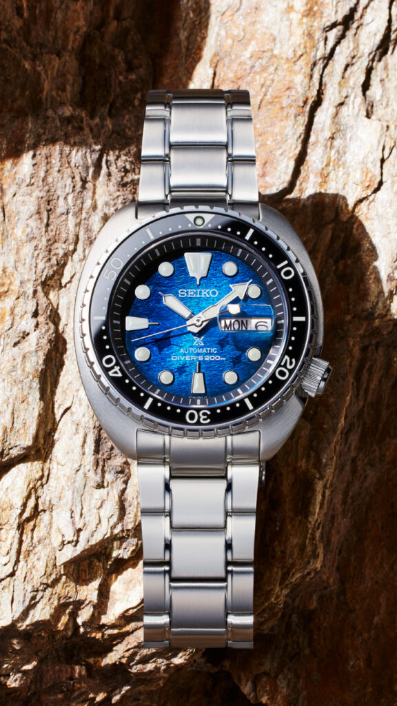 La imagen presenta el reloj SEIKO SRPE39K sobre un fondo de piedra/madera en un ambiente de día. Es uno de los modelos de la "selección de relojes favorita del propietario de AlphaWatches&Co."