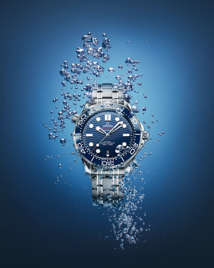 La imagen presenta el reloj Omega Diver m300 de color azul sobre el fondo azul oscuro para dar efecto de que está metido en el agua. Es uno de los modelos de la "selección de relojes favorita del propietario de AlphaWatches&Co."